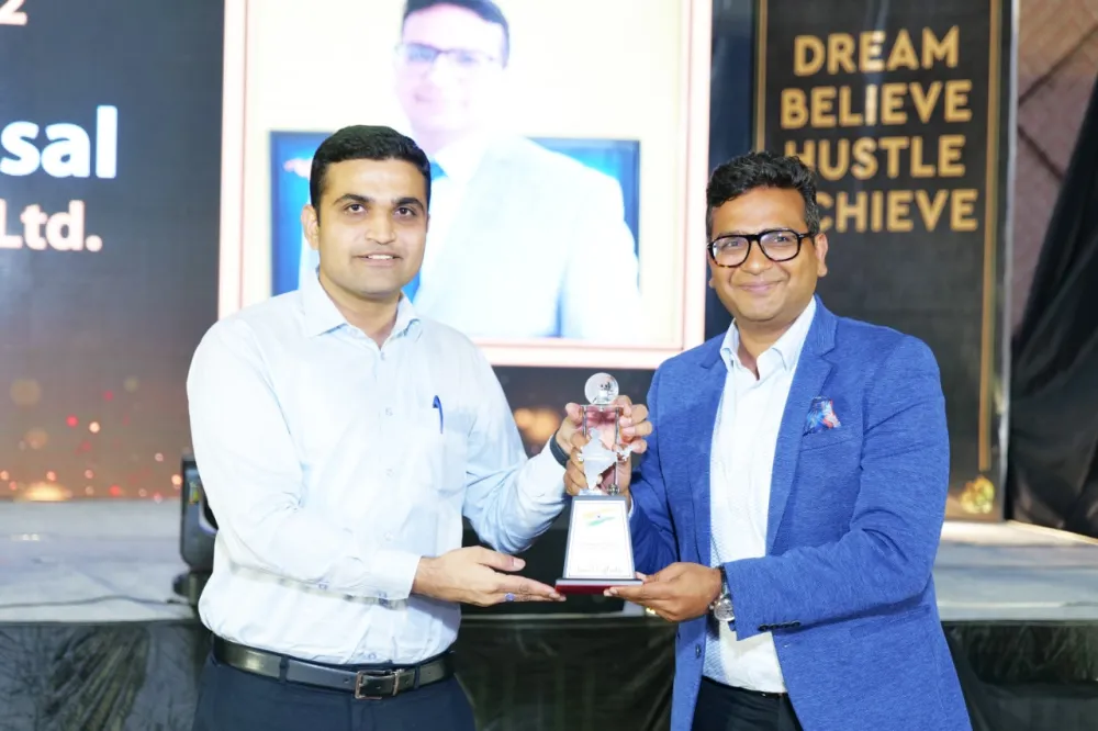 Two men holding a trophy on stage at an awards event, with a 'Dream Believe Hustle Achieve' sign behind them